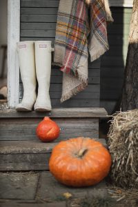 Rustic porch scene with pumpkins, plaid blanket, and boots showcasing a cozy fall atmosphere.